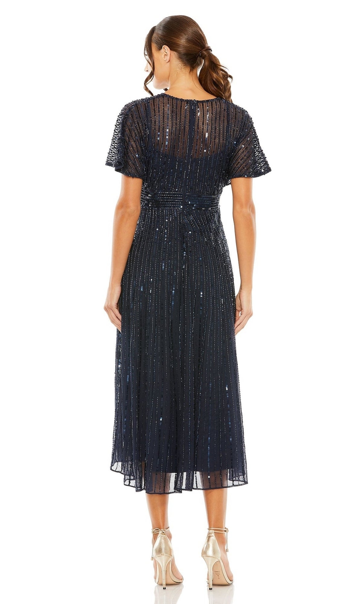 A woman faces away in the Mac Duggal 14007—a navy blue short sequin dress with short sleeves and vertical sequin detailing, styled with metallic heels. Ideal as a semi-formal or wedding-guest dress.